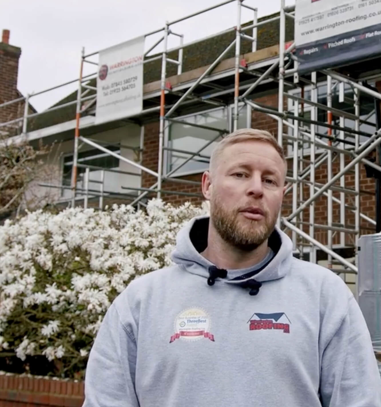 A Warrington Roofing Ltd roofer on site in front of a scaffolded roof
